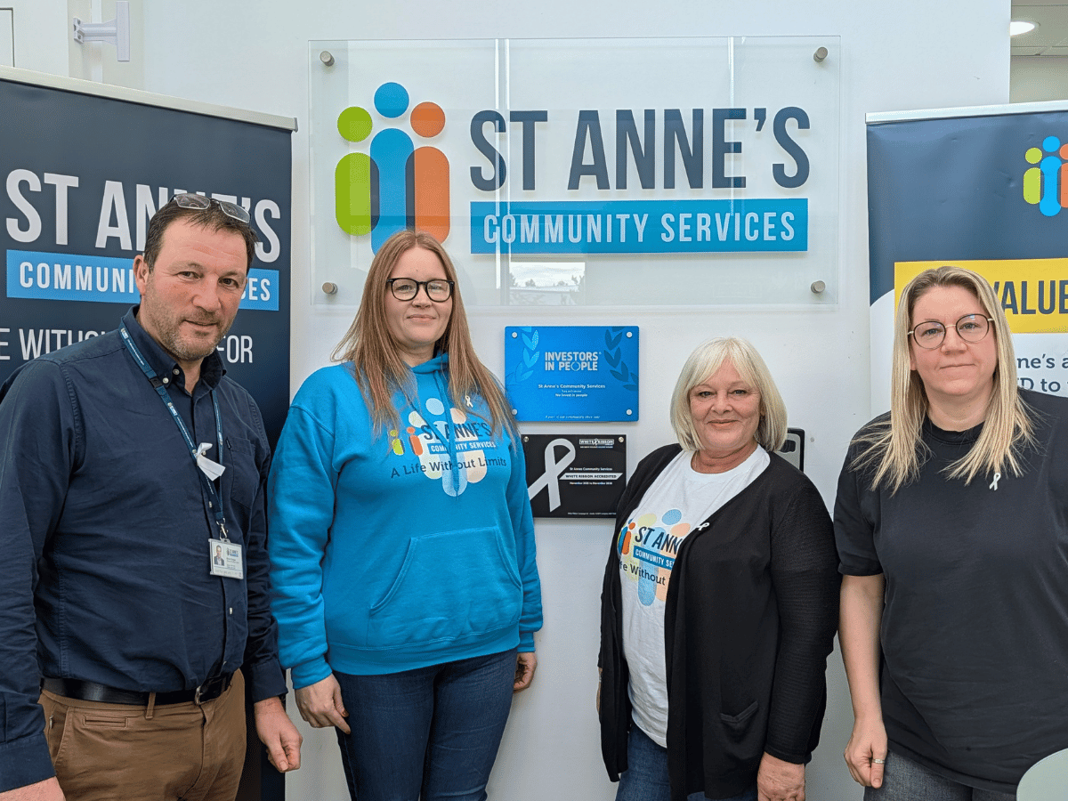 Four people standing in front of a St Annes sign proudly smiling because the have just added the white ribbon plaque to the office entryway